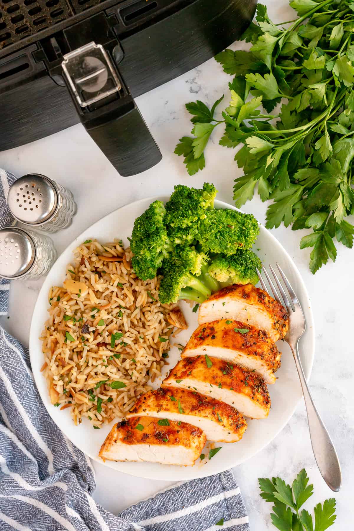 An over the top shot of cooked, sliced chicken on a plate in front of an air fryer.