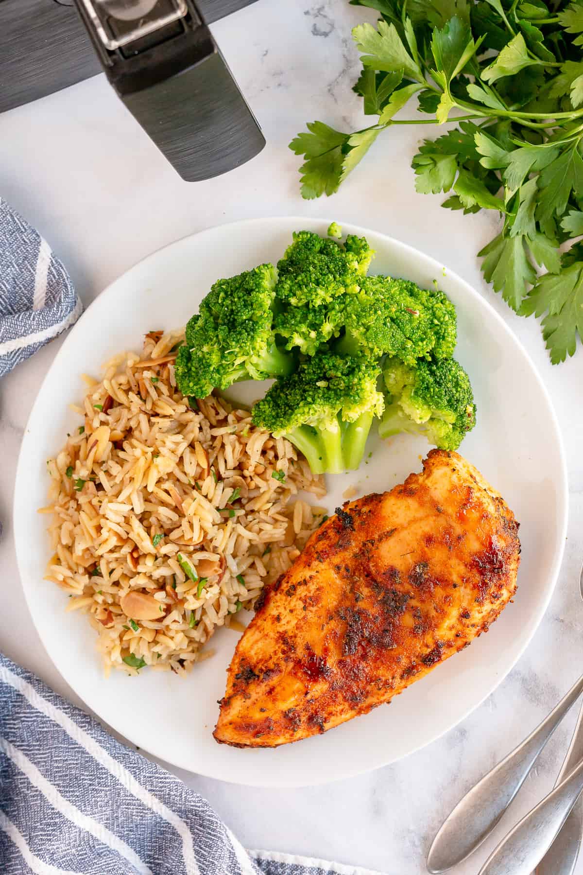 An air fried chicken breast on a white plate with broccoli and rice.