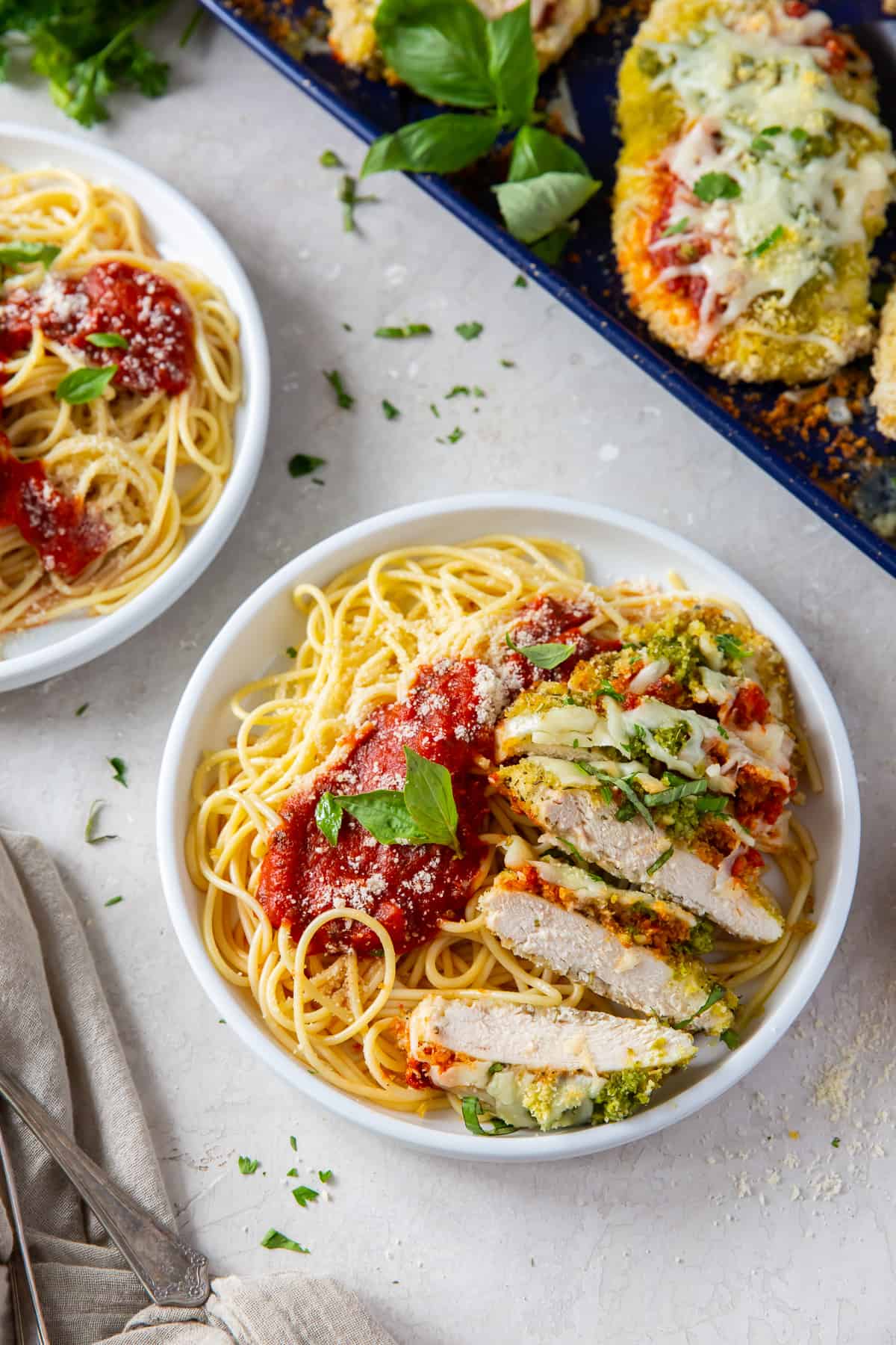 Sliced Chicken Pesto Parmesan in a white dish with pasta and marinara sauce.