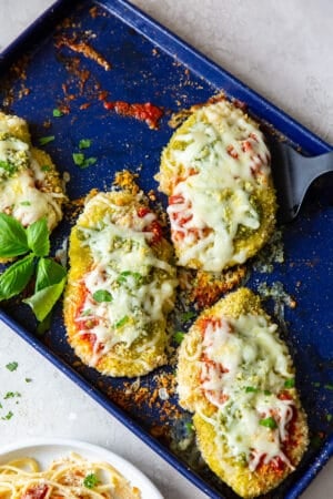 Baked Chicken Pesto Parmesan on a blue baking sheet.