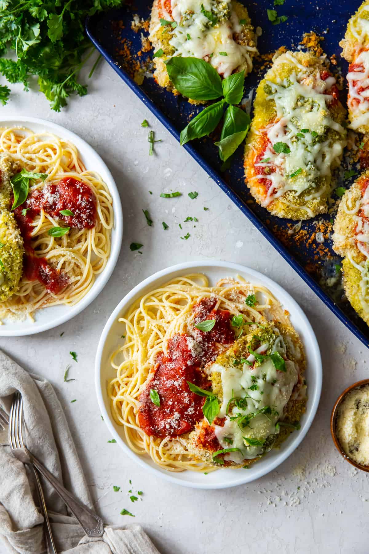 An over the top shot of chicken pesto parmesan with pasta on white plates.