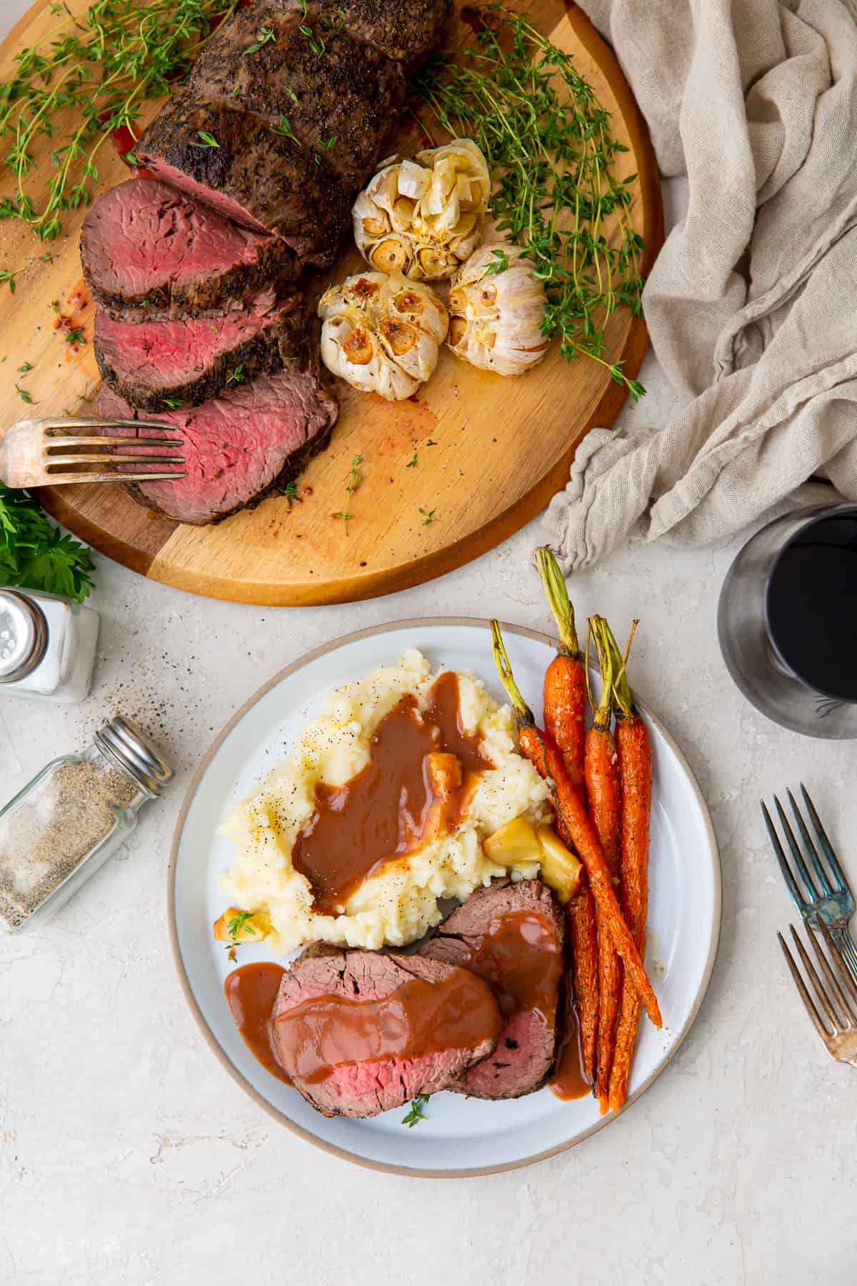 An over the top shot of beef tenderloin with gravy on a plate with mashed potatoes and carrots.