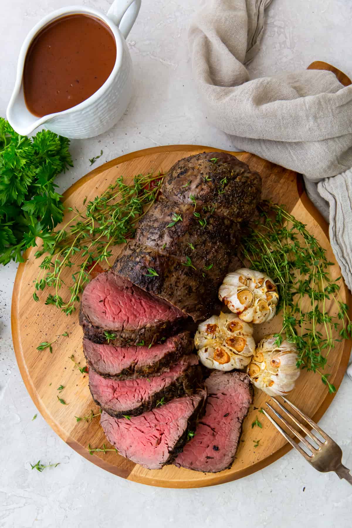 A sliced beef tenderloin on a wood platter with roasted garlic.