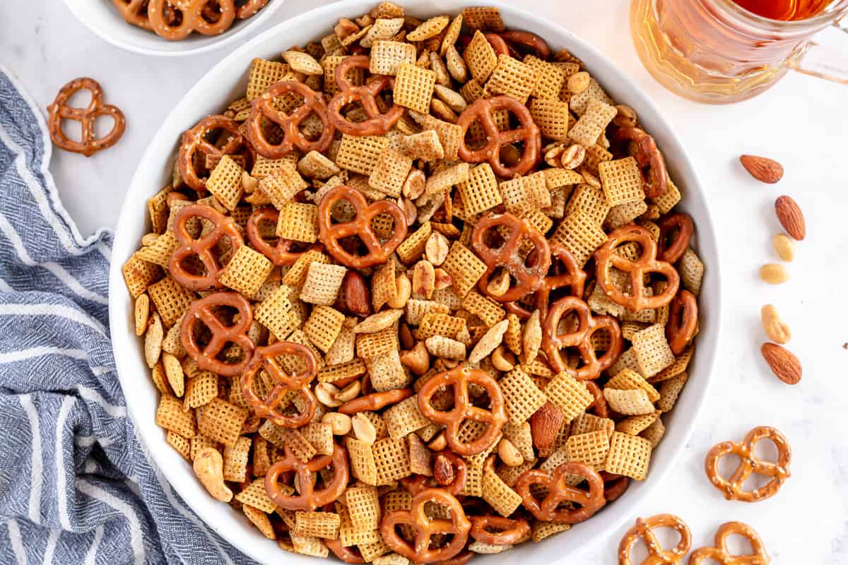A white bowl filled with Chex cereal, nuts, and pretzels.