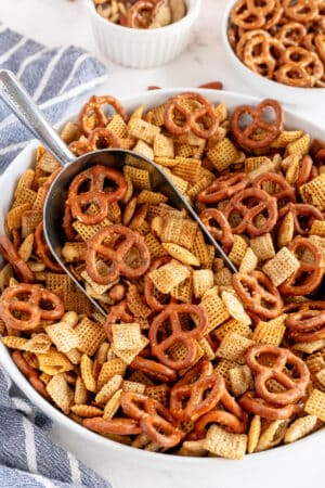 A metal scoop resting in a bowl of Chex Mix.