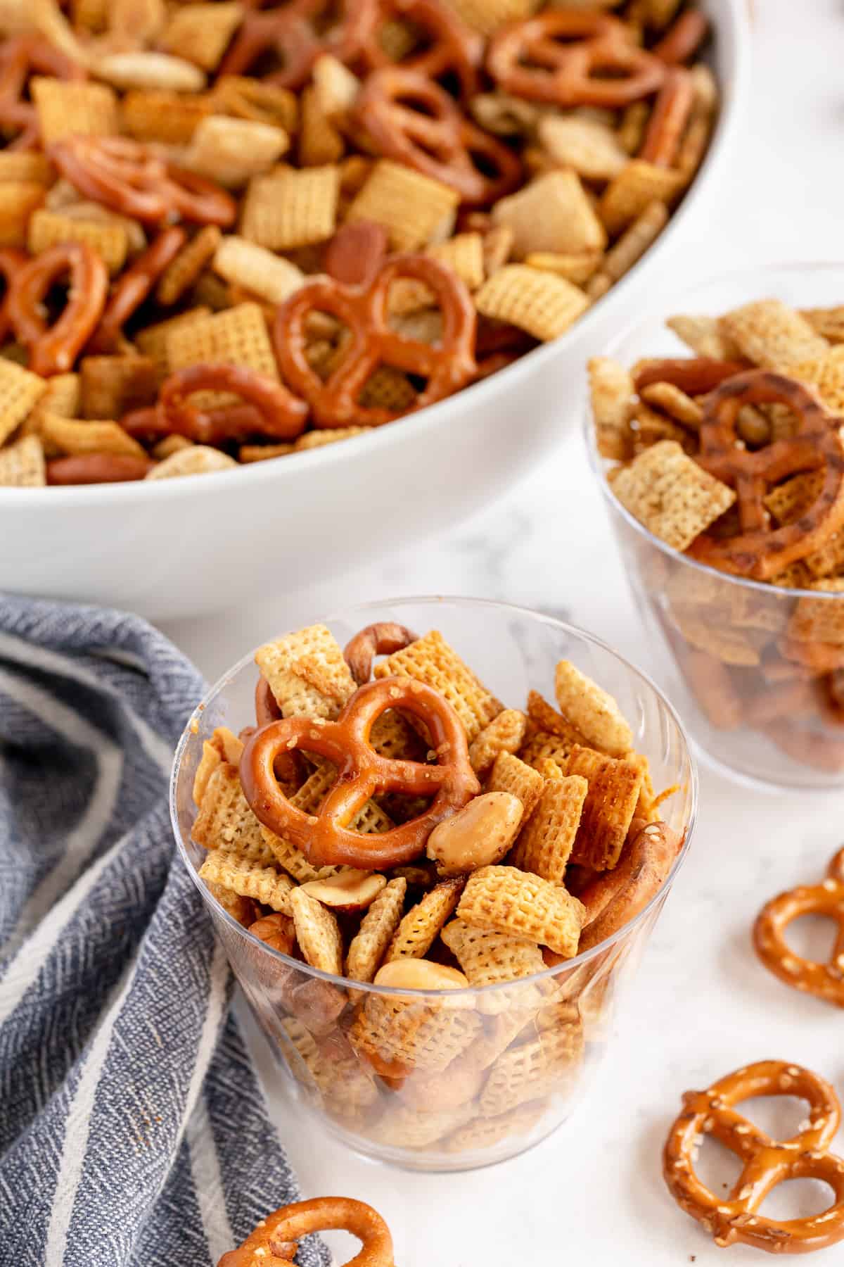 A clear plastic cup filled with Chex Party Mix.