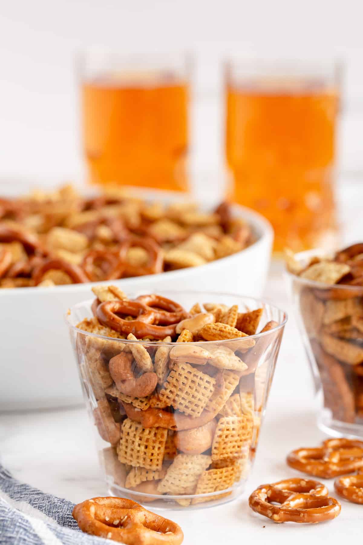 A side view of a plastic cup of Chex Mix with beers in the background.