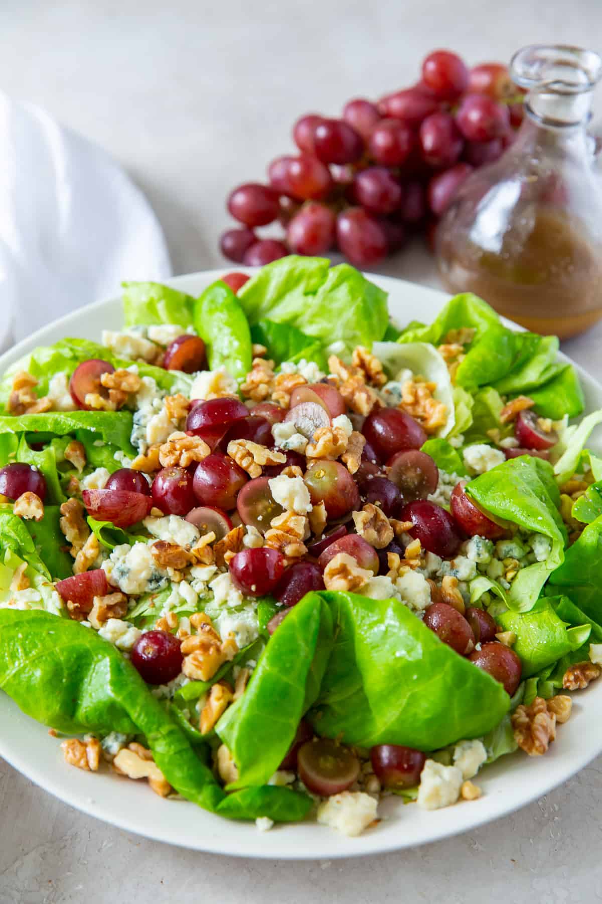 Butter lettuce salad with grapes and walnuts on a white plate with grapes in the background.