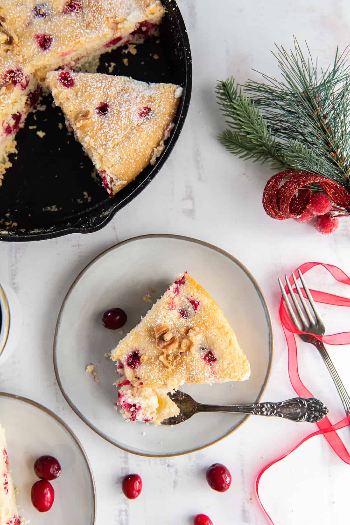 An over the top shot of a skillet cranberry cake next to a plate with a slice.