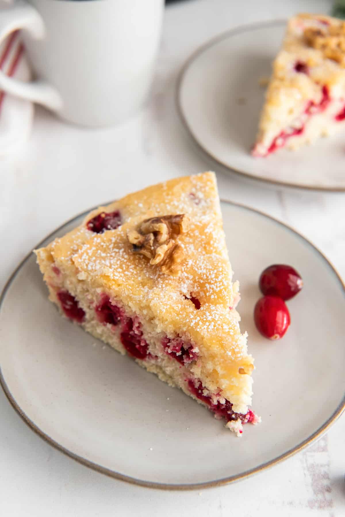 A slice of cranberry cake on a plate with fresh cranberries.