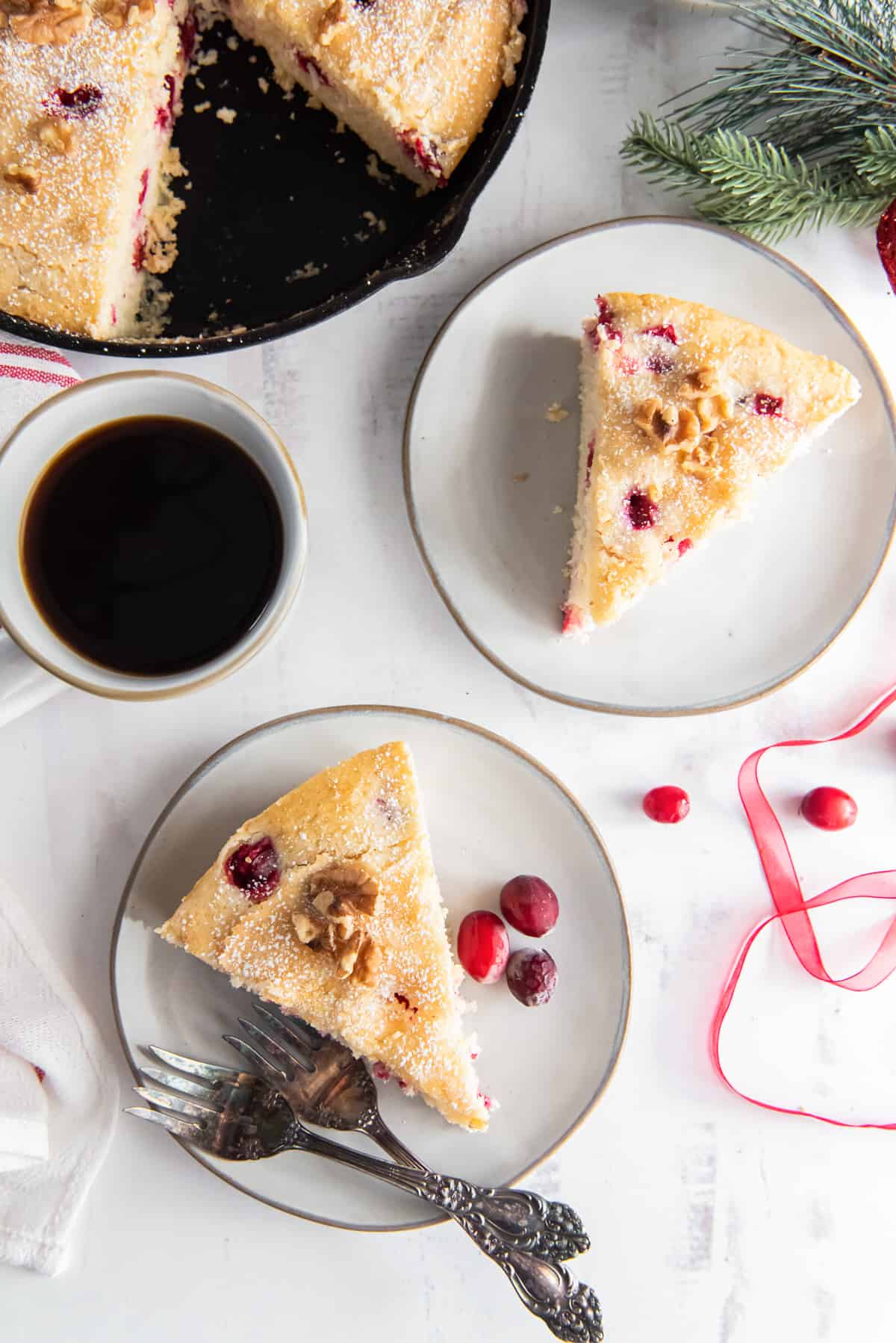 Slices of cranberry cake on plates next to a cup of coffee.