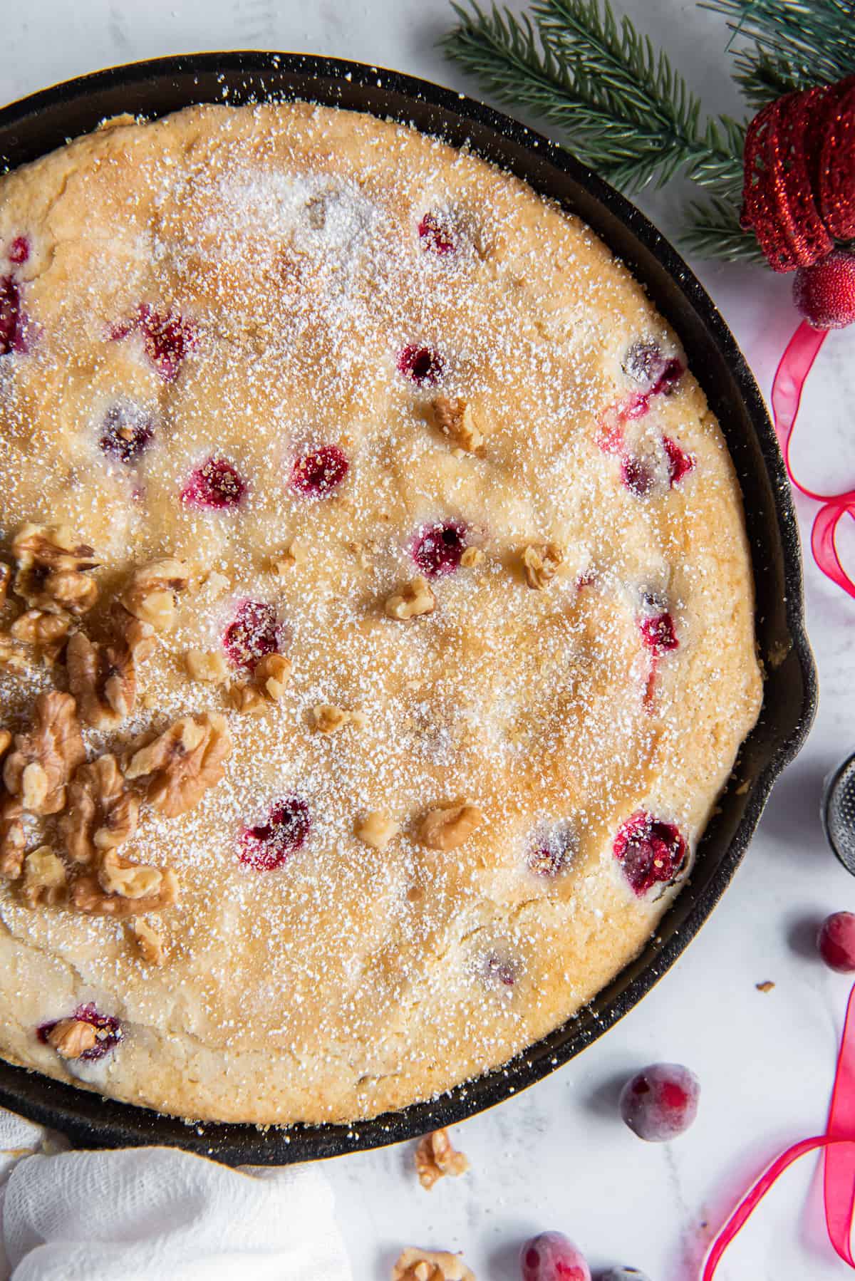 A close up over the top shot of cranberry breakfast cake in a cast iron skillet topped with powdered sugar.
