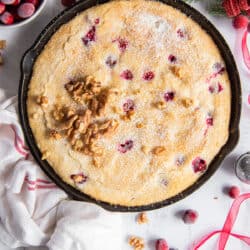 An over the top shot of cranberry cake in a cast iron skillet wrapped with a kitchen towel.