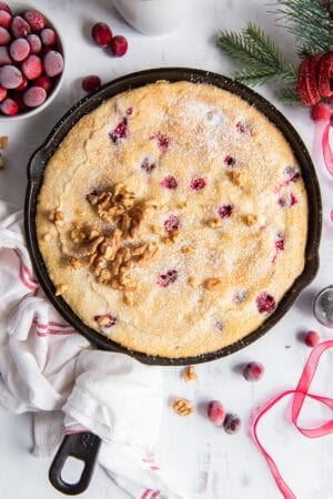 An over the top shot of cranberry cake in a cast iron skillet wrapped with a kitchen towel.