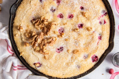 An over the top shot of cranberry cake in a cast iron skillet wrapped with a kitchen towel.