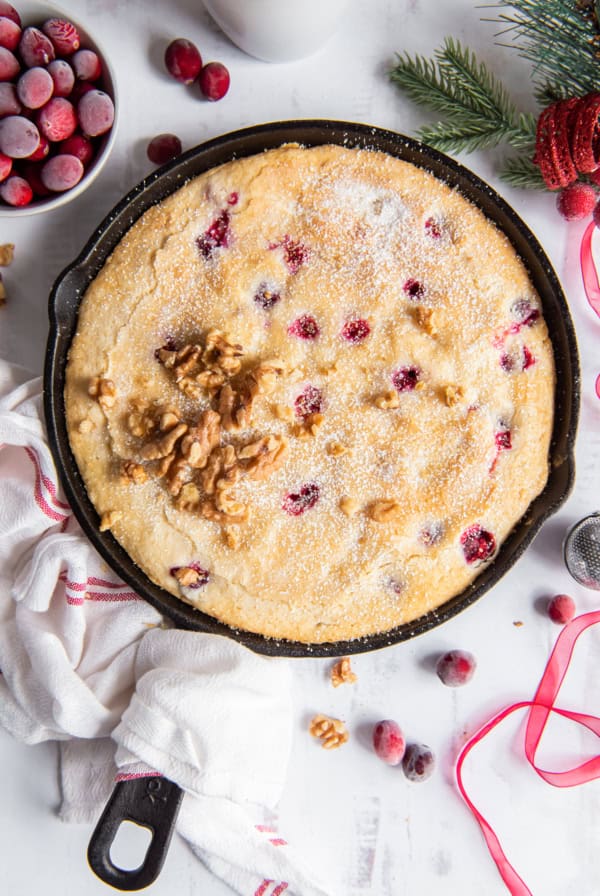 An over the top shot of cranberry cake in a cast iron skillet wrapped with a kitchen towel.