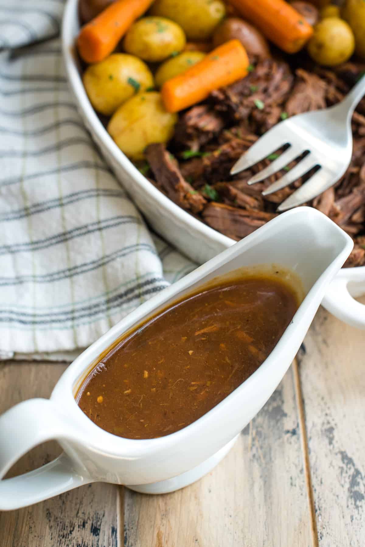 The gravy for the Instant Pot Pot Roast in a white gravy boat.