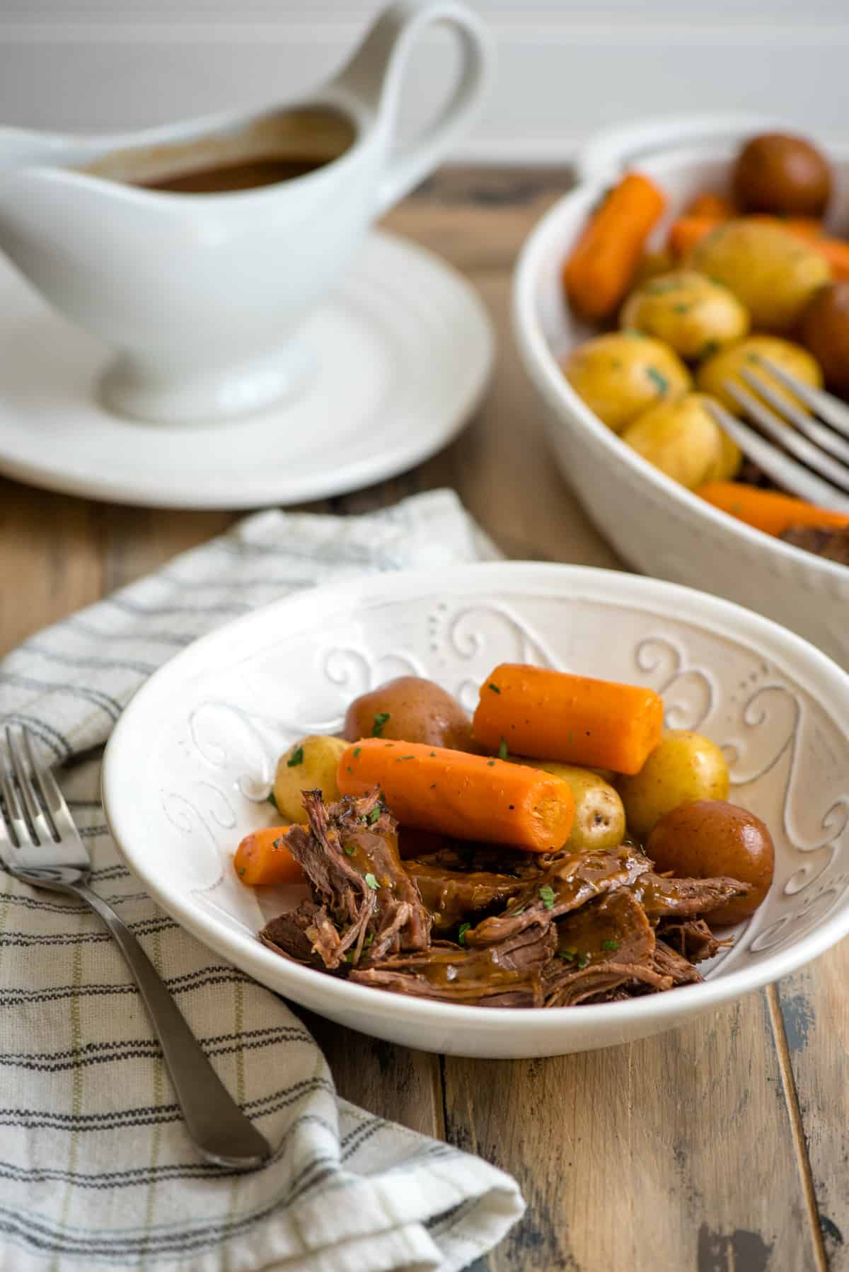  A serving of pot roast with carrots and potatoes in a white bowl.