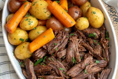 An over the top shot of pot roast, carrots and potatoes in a white dish.