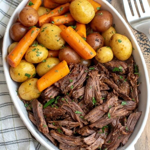 An over the top shot of pot roast, carrots and potatoes in a white dish.