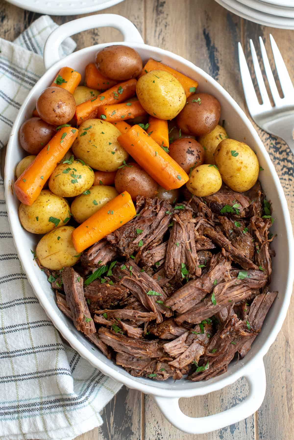 An over the top shot of pot roast, carrots and potatoes in a white dish.