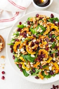 Roasted delicata squash salad in a white bowl with balsamic vinaigrette behind it.