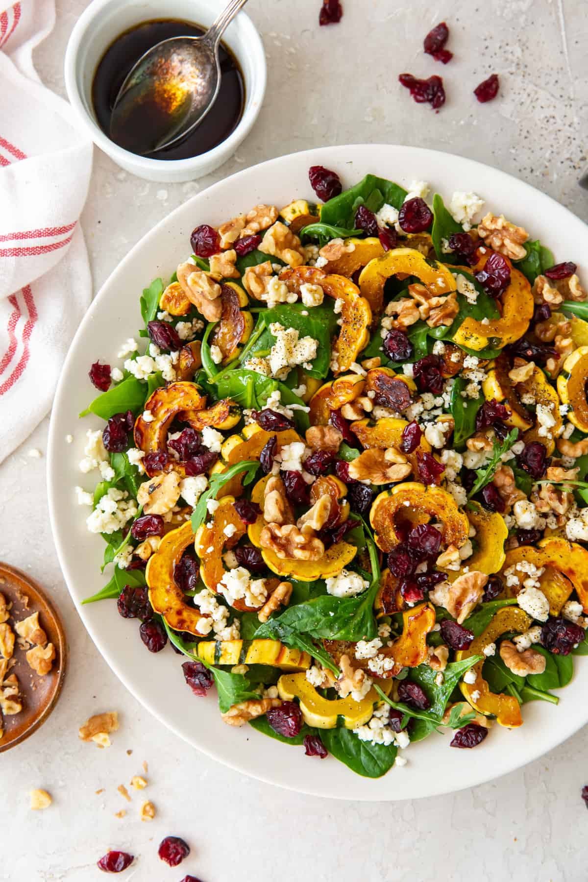 Roasted delicata squash in a white bowl with greens, cranberries and feta.