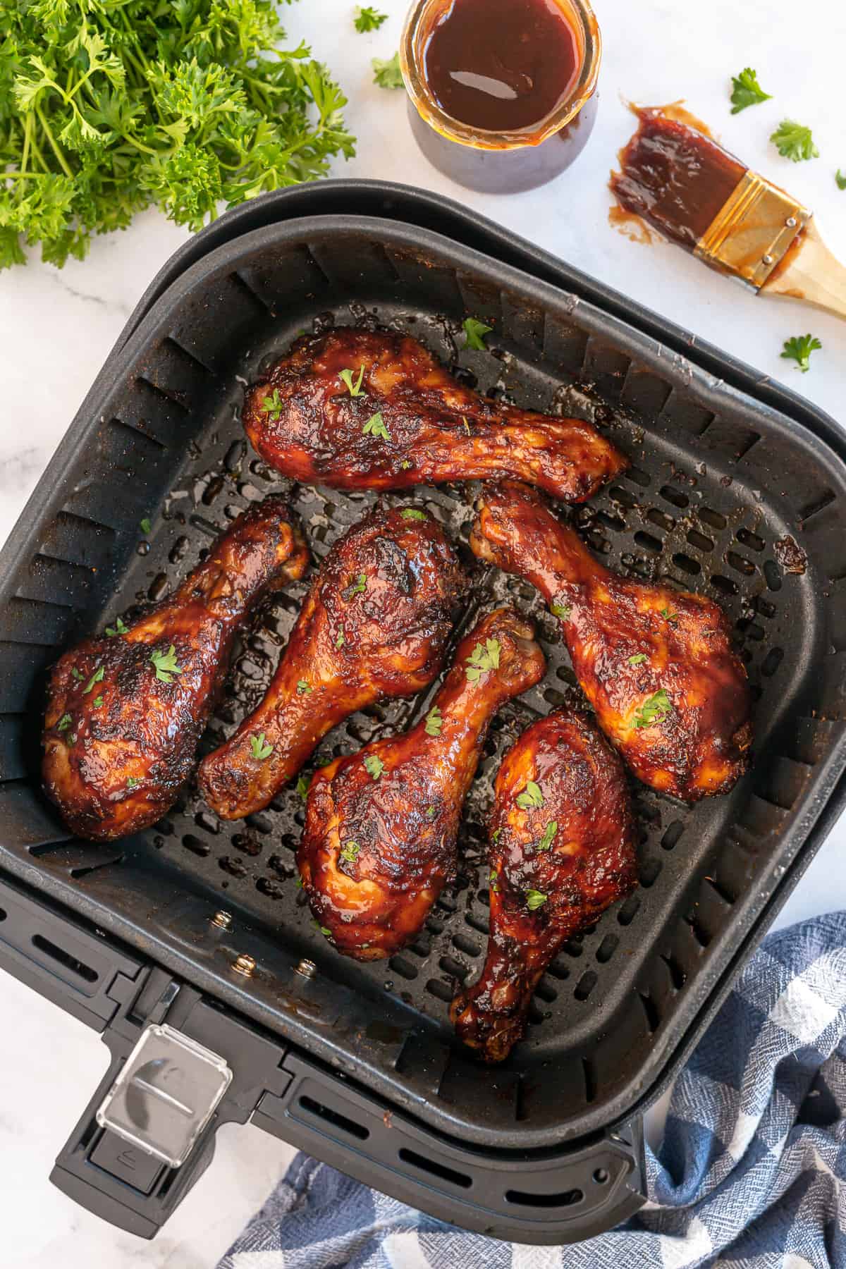 An over the top shot of an air fryer basket filled with BBQ chicken drumsticks.