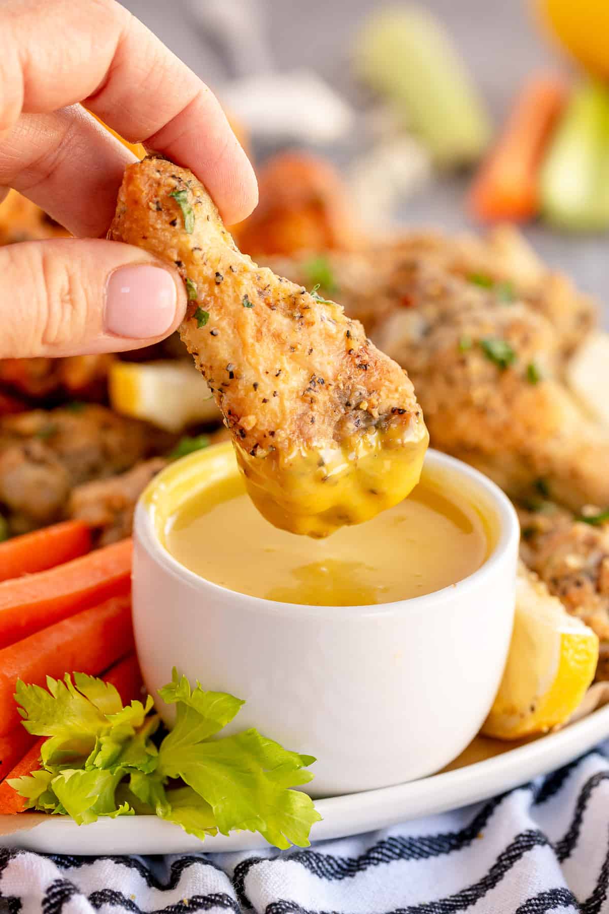 A lemon pepper wing dipping into honey mustard dipping sauce.