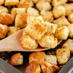 A spoon lifts croutons from a baking sheet.