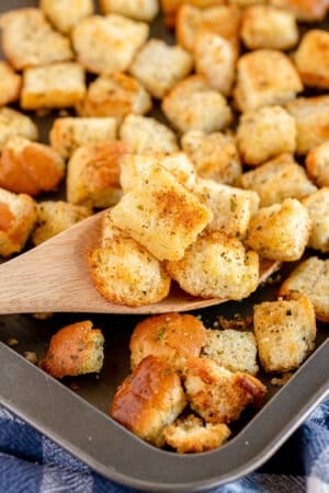A spoon lifts croutons from a baking sheet.
