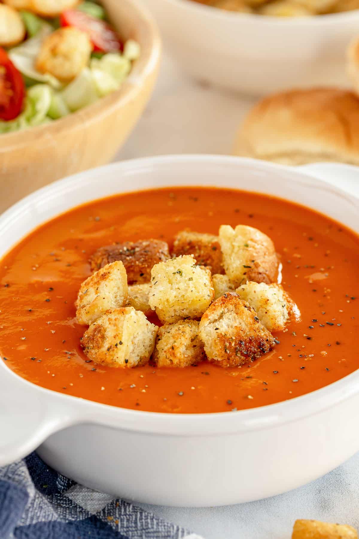 A close up of tomato soup topped with croutons in a white bowl.