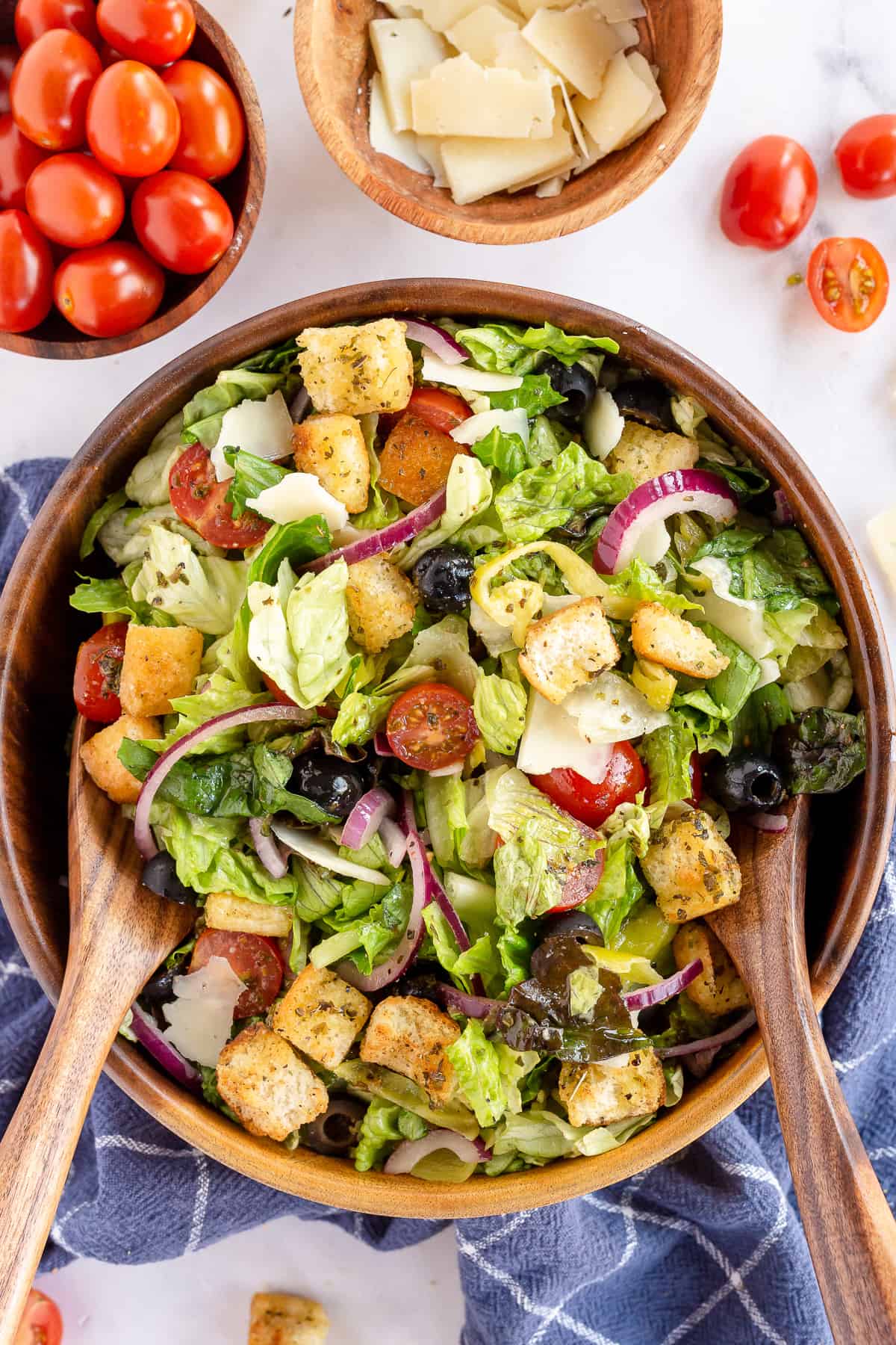 An over the top shot of a green salad with salad in a wood bowl with salad spoons.