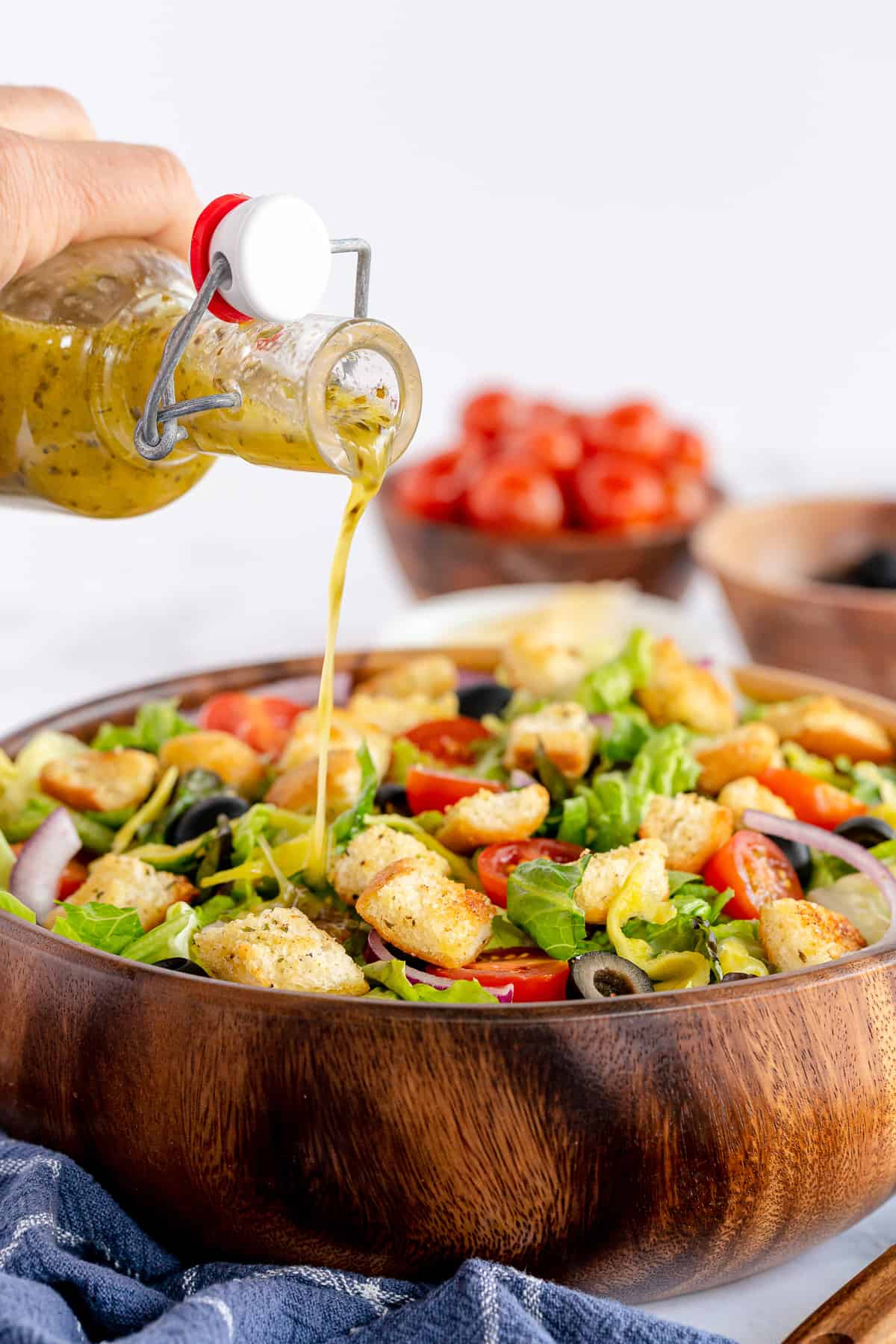 Italian dressing pouring from a bottle on to a salad in a wood bowl.