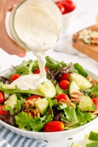 Blue cheese dressing pours from a mason jar on to a salad in a white bowl.