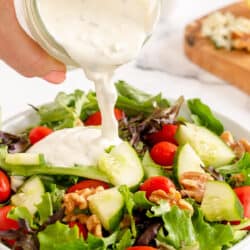 Blue cheese dressing pours from a mason jar on to a salad in a white bowl.