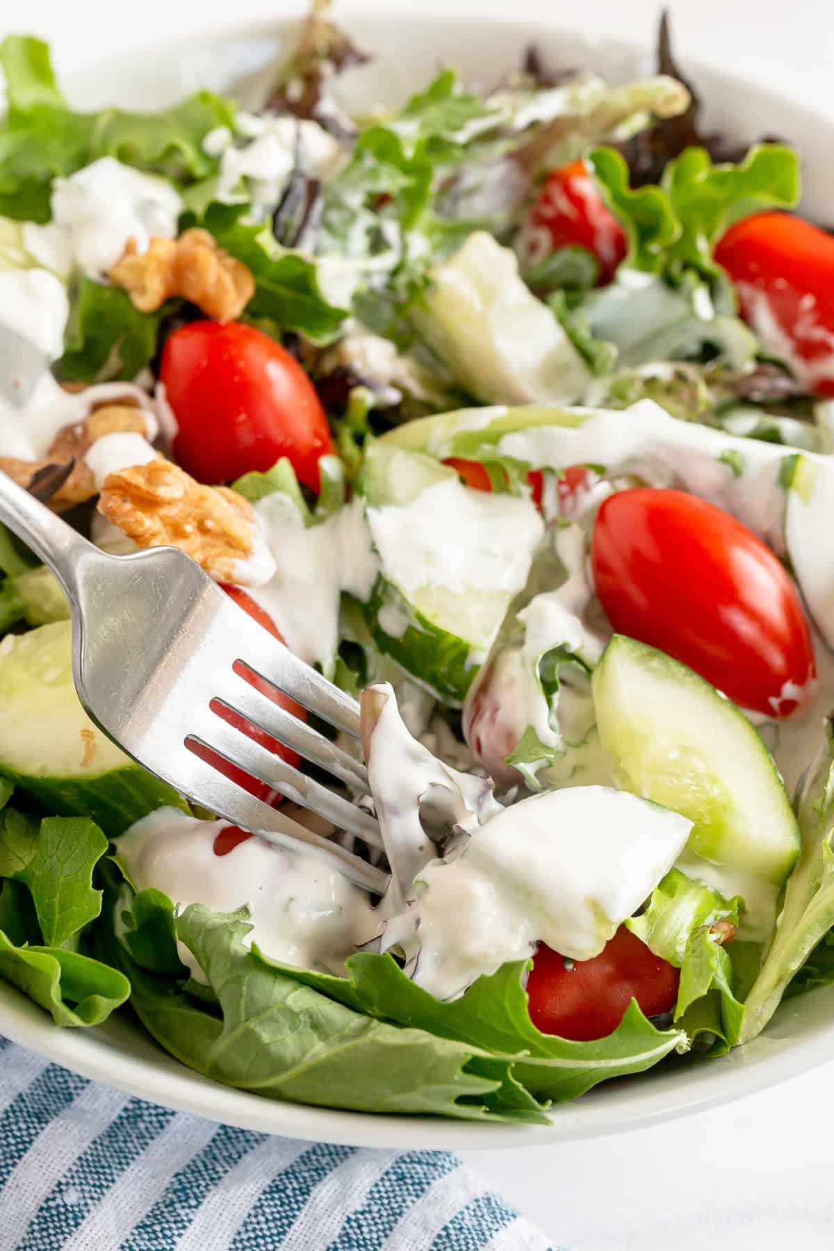 A fork digs into a salad with light blue cheese dressing.