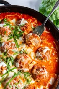 An over the top shot of a fork piercing a turkey meatball in a skillet.