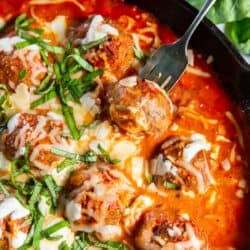 An over the top shot of a fork piercing a turkey meatball in a skillet.