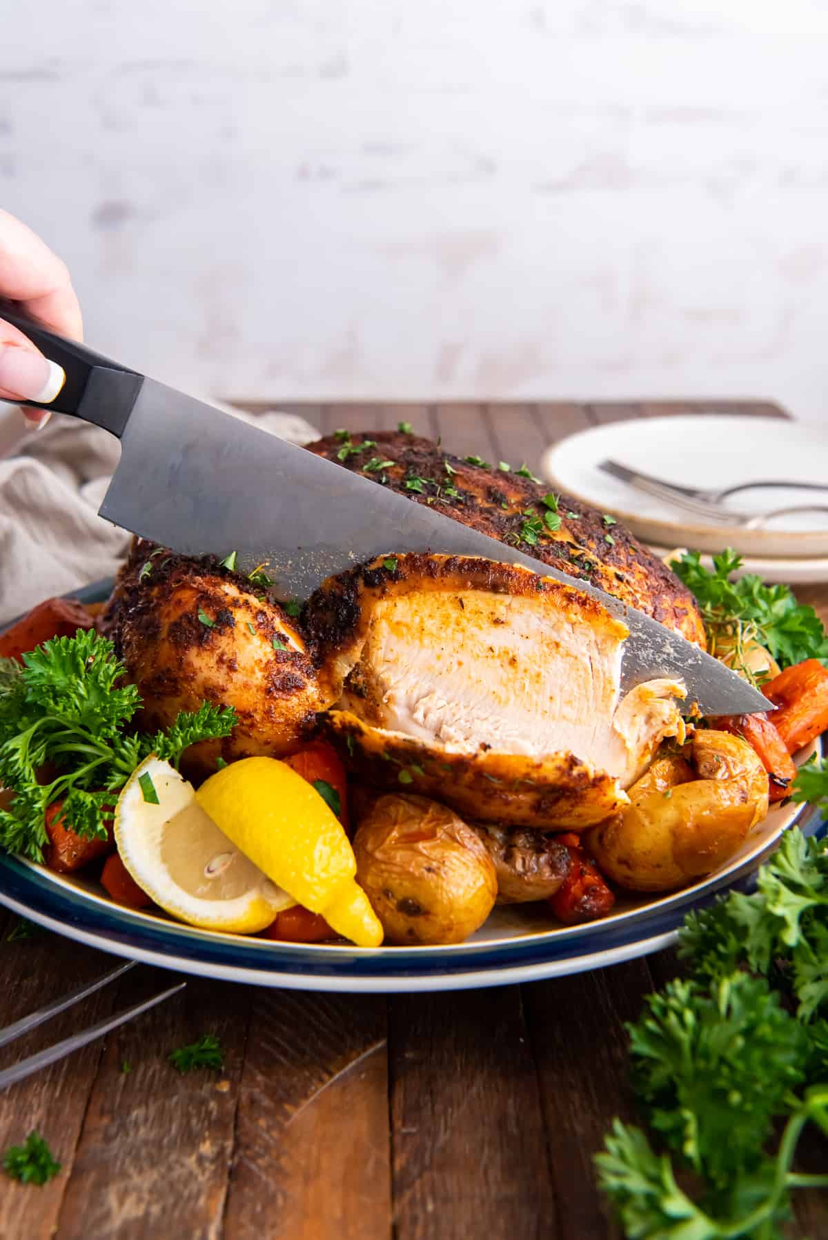A knife slices into the breast meat of a whole roasted chicken.