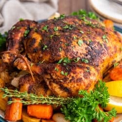 A crispy roast chicken on a platter with carrots and potatoes.