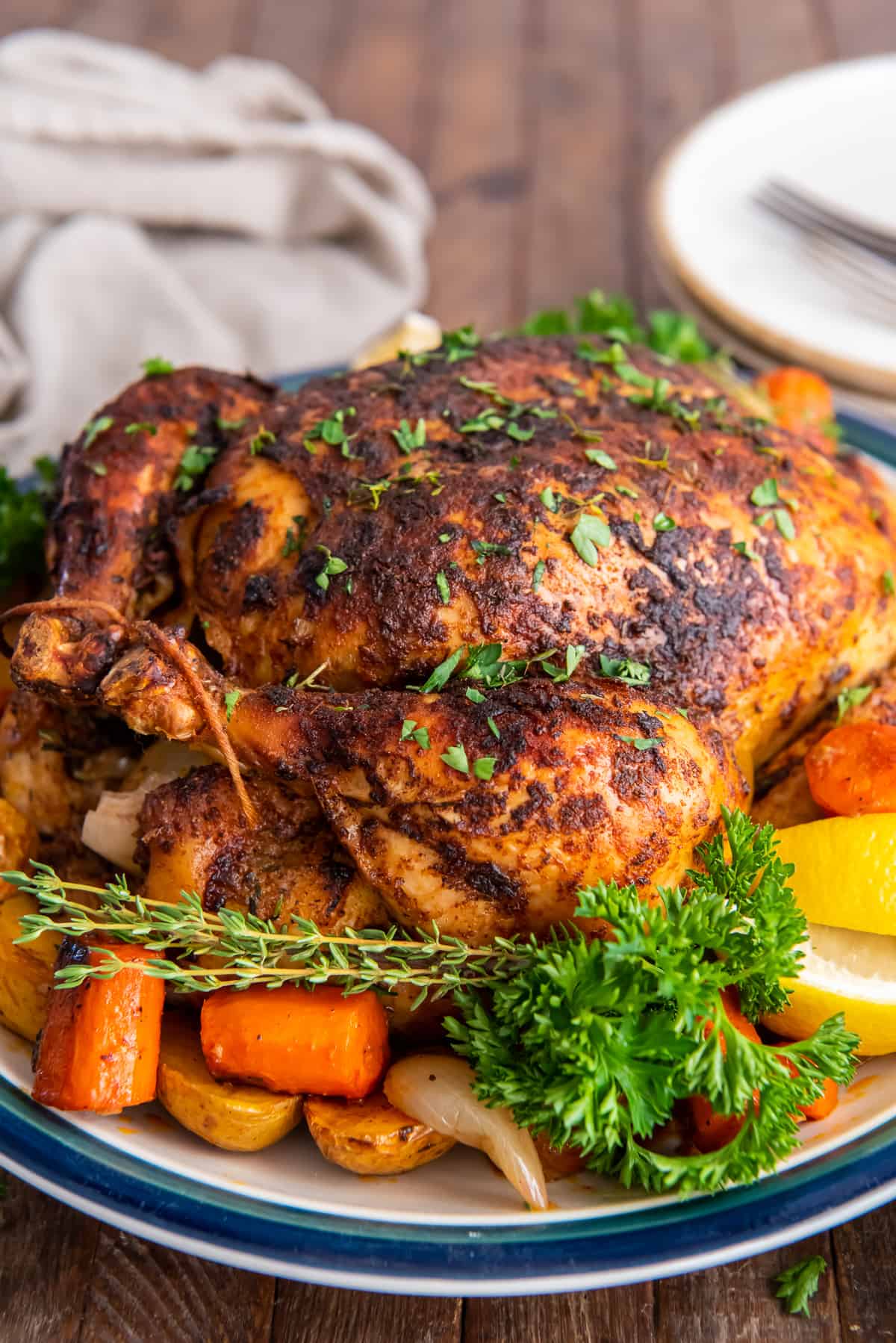 A crispy roast chicken on a platter with carrots and potatoes.