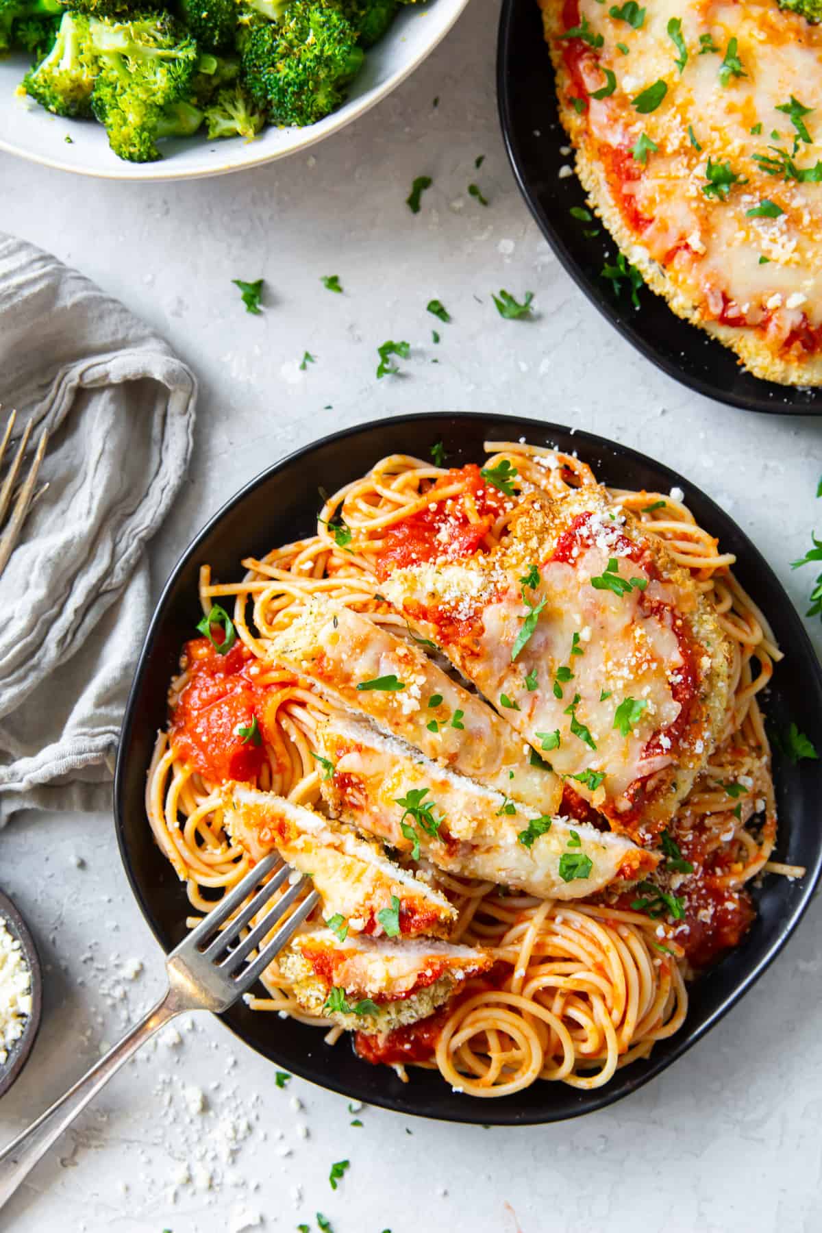 An over the top shot of sliced chicken parmesan on a black plate with a fork.