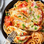 A fork piercing a slice of chicken parmesan on a black plate.