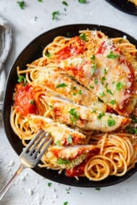 A fork piercing a slice of chicken parmesan on a black plate.