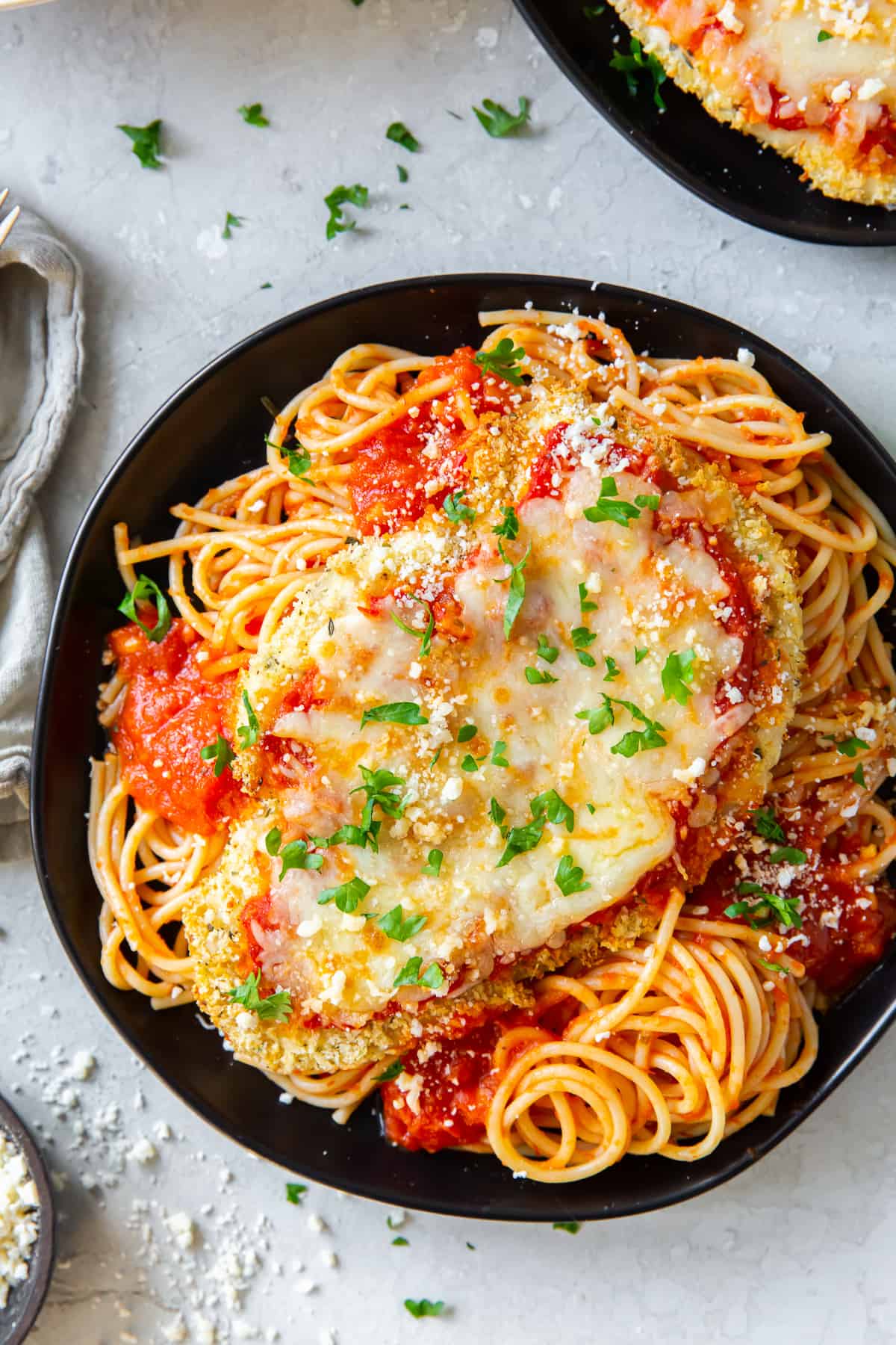 An over the top shot of Chicken Parmesan and pasta on a black plate.