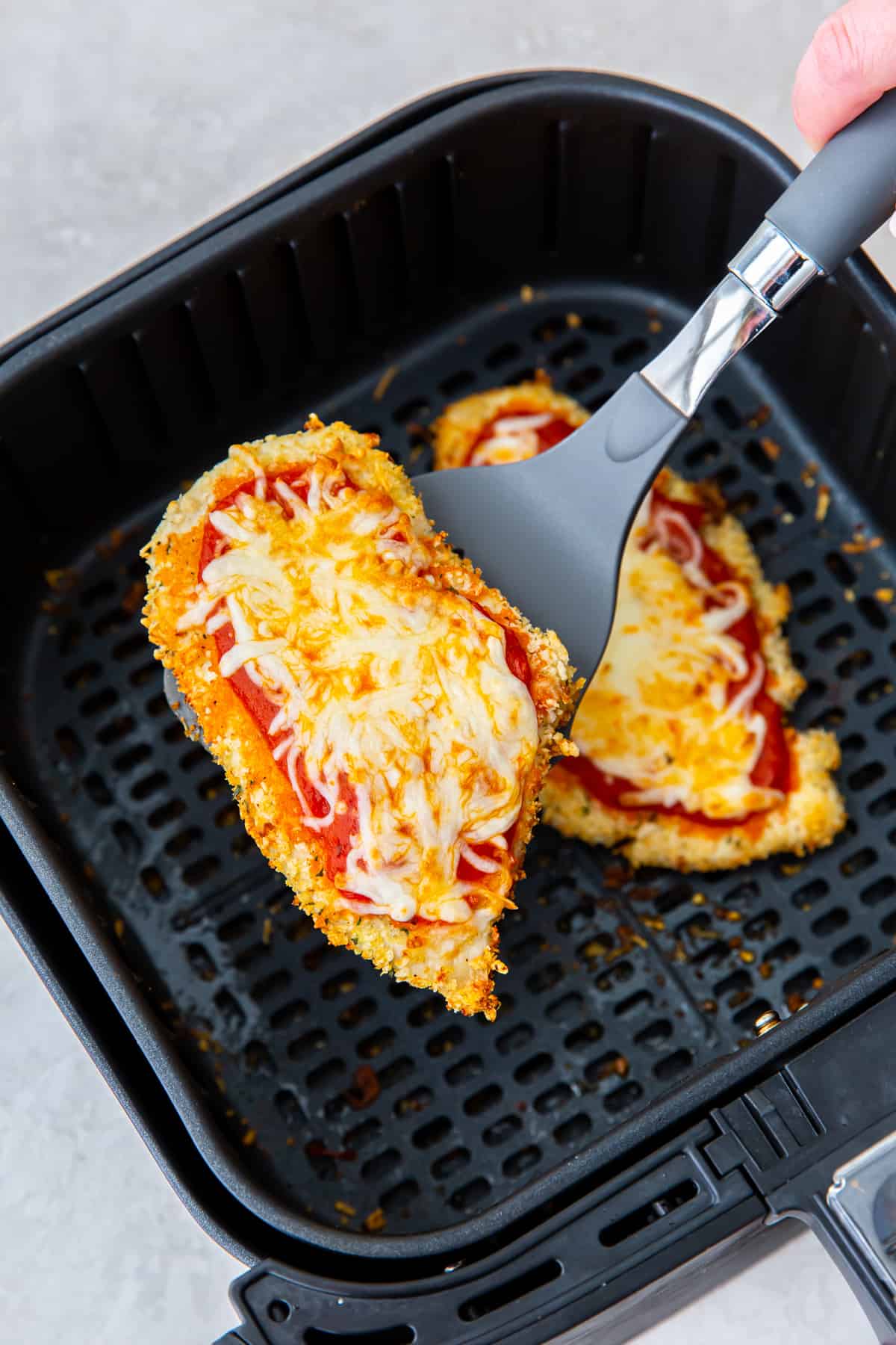 A spatula lifts chicken parmesan from an air fryer.