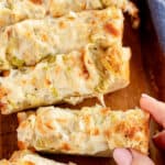 A hand taking a piece of Cheesy Artichoke Bread.