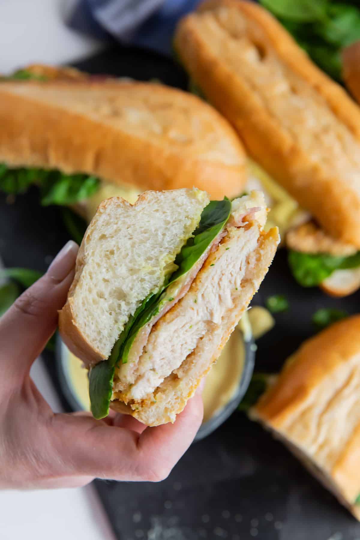 A hand holds a sliced Chicken Cordon Bleu Sandwich up towards the camera.