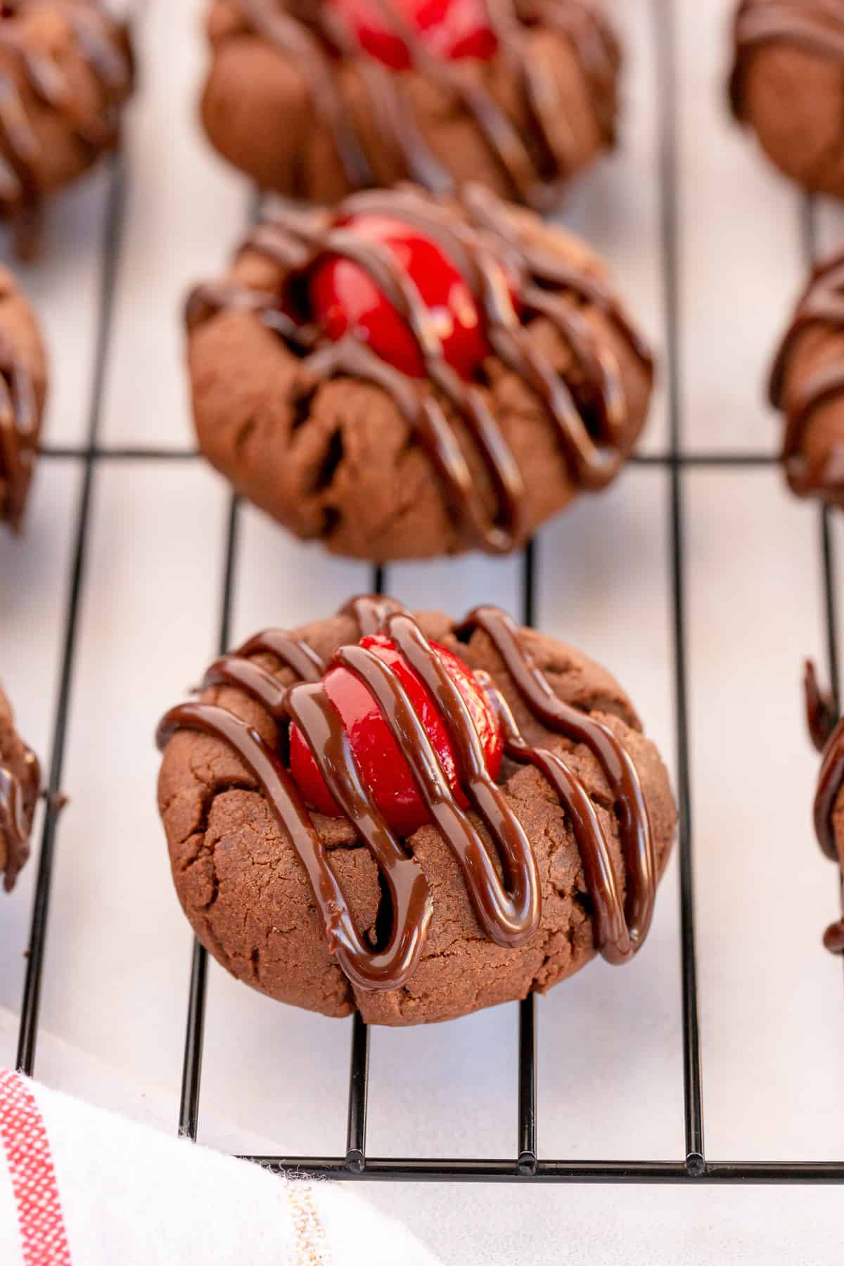 Chocolate cherry cookies with frosting on a wire rack.